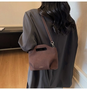 Detail view of brown suede bucket bag with oval handle and adjustable shoulder strap