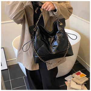 Detail view of large black quilted tote bag with chain strap shown in lifestyle setting