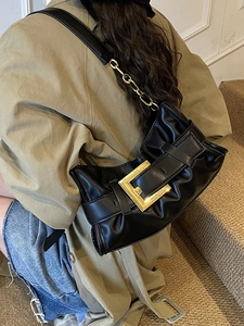 Ruched black leather shoulder bag with gold buckle and chain strap on a trench coat model