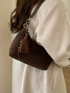 Retro dark brown suede crescent shoulder bag with tassel detail on a beige wool coat
