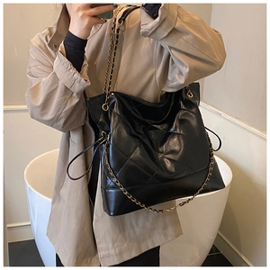 Classic black quilted tote bag with gold chain strap shown on khaki trench coat
