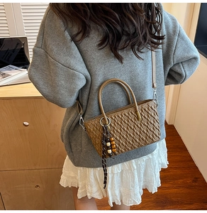 Braune Handtasche mit Webstruktur, Doppelgriffen und Holzperlen-Anhänger auf einem Tisch