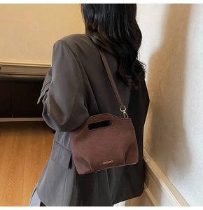Close-up of brown suede bucket bag with cut-out handle and metallic logo detail