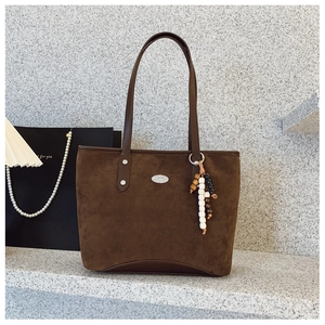 Détail d'un sac cabas en daim marron avec pendentif en bois et logo en métal argenté