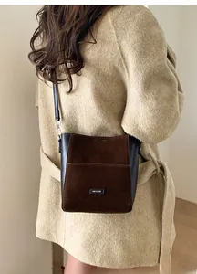 Détail du sac seau en daim marron et cuir noir porté sur un manteau en laine beige