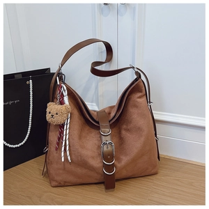 Close-up of brown suede tote bag with leather buckle and cute teddy bear pendant detail