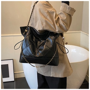Detailed view of black quilted leather hobo bag with gold chain strap on shoulder
