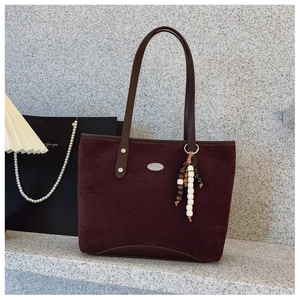 Détail du sac cabas en daim bordeaux avec breloque en perles de bois de style ethnique et logo