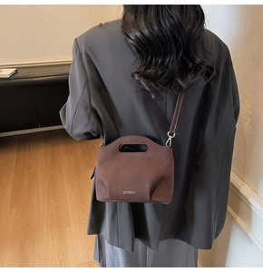 Detail of brown suede bucket bag with cut-out handle and gold metal hardware