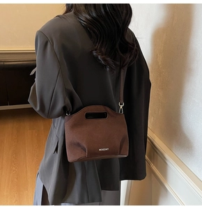 Detail of a brown suede bucket bag with cut-out handle and white MOEDNT lettering logo