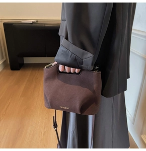 Detail of a dark brown suede bucket bag with gold logo and adjustable shoulder strap