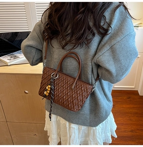 Detailansicht der braunen Bucket-Bag mit Webstruktur und dekorativem Holzperlen-Anhänger