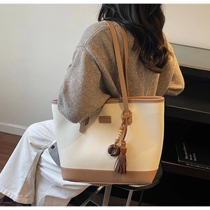 Detail of cream and brown tote bag featuring lychee leather texture and retro tassel charm