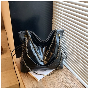 Macro shot of large black quilted tote bag with chain strap on white books