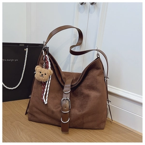 Detailed view of brown tote bag with bear charm on light wooden floor setting