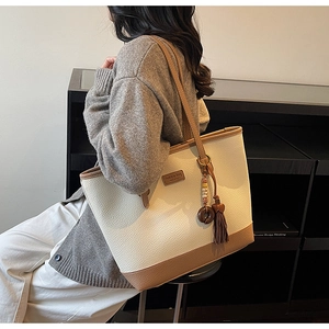 Macro detail of cream lychee texture tote bag with brown straps and tassel charm