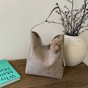 Détail du sac hobo en daim taupe avec charme d'ours sur une table en bois minimaliste