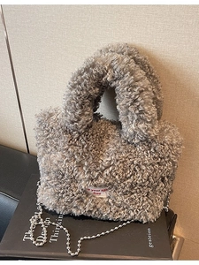 Secchiello chic in peluche grigia con tracolla a catena su sfondo di libro d'arte