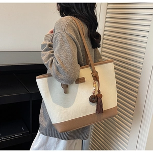 Close-up of white lychee leather tote bag with brown tassel and beaded charm detail