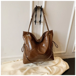 Detail of brown quilted tote bag with golden metal chain strap and glossy PU leather texture