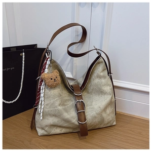 Detail view of the textured beige tote bag with brown leather straps and a plush bear charm