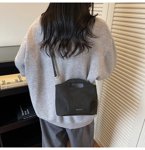 Detail of a black matte bucket bag with oval cutout handle worn as a crossbody bag