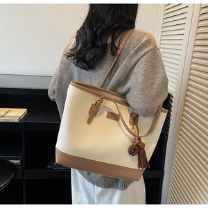 Detail of cream pebbled tote bag with dark brown tassel charm and leather trim