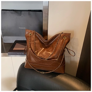 Macro shot of large brown quilted tote bag with gold chain strap on a black chair