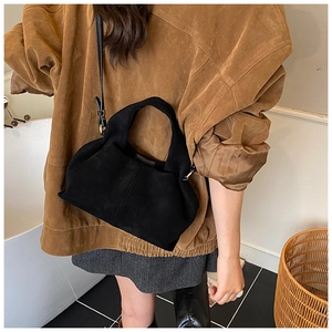 Detail of minimalist black matte bucket bag in suede fabric worn as a shoulder bag