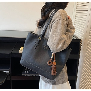 Close-up of black pebble leather tote bag featuring a tassel charm and metal logo plaque