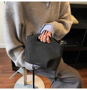 Detail of black matte bucket bag featuring oval cutout handle and gold logo print
