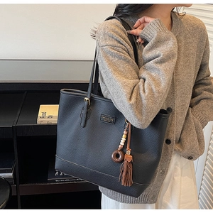 Detail of black pebbled leather tote bag with ethnic tassel charm and metal logo tag