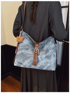 Model wearing a large light blue canvas tote bag with brown leather straps and bear charm