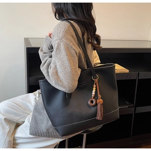Close-up of black lychee-grain leather tote bag with wooden ring and tassel charm detail