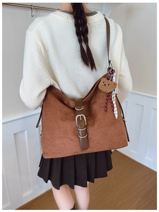 Brown suede tote bag detail featuring dark leather straps and plush bear charm