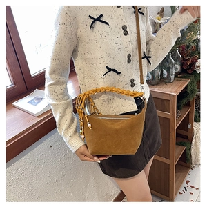 Detail of a brown suede crossbody bag featuring a braided handle and long beaded tassels