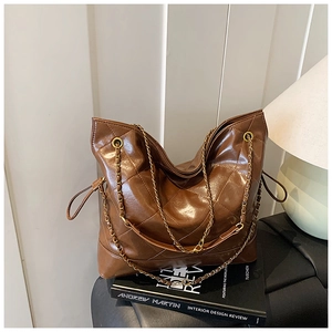 Detail of a brown quilted leather tote bag featuring gold chain straps and drawstring sides