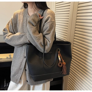 Detail of black tote bag featuring textured leather, logo tag, and retro tassel pendant