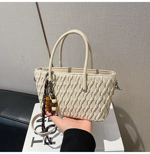 Detailansicht der cremefarbenen Handtasche mit Webstruktur und Holzperlenanhänger