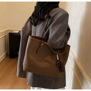 Detail showing the brown lychee leather texture and vintage tassel on the tote bag