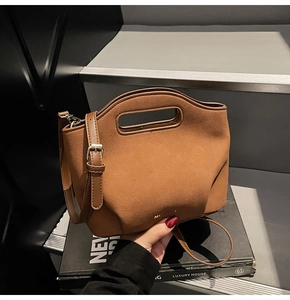 Detail of brown suede bucket bag with integrated cutout handle and gold logo