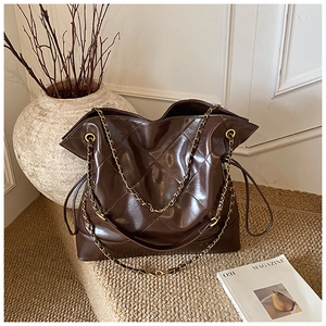 Detail of dark brown quilted tote bag with golden chain straps and glossy finish texture