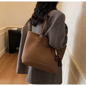 Brown leather tote bag with tassel charm and gold buckle on a gray wool coat model