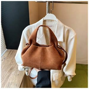 Macro detail of brown suede bucket bag featuring contrast stitching and leather strap