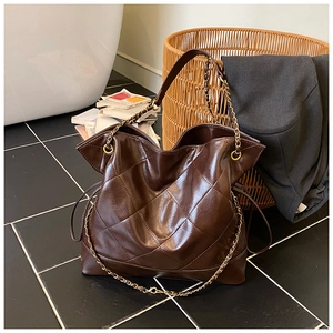 Detail view of large dark brown tote bag with quilted diamond pattern and chain handles