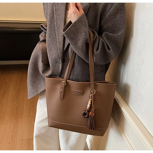 Detail view of brown lychee-grain leather tote bag with tassels and gold buckle