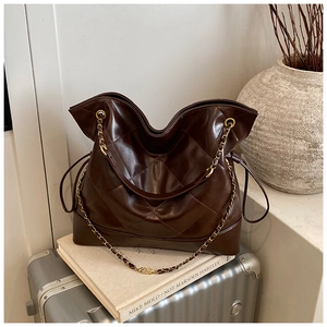 Macro detail of dark brown quilted tote bag with golden metal chain strap and stitching