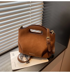 Close-up of brown suede bucket bag with oval handle and golden metal logo detail