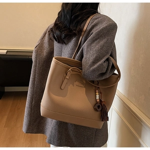 Detail of camel lychee leather tote bag featuring brown tassel charm and shoulder strap