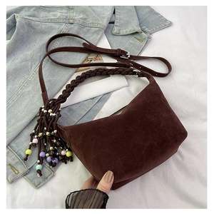 Detail of woven handle and colorful beaded tassel on dark brown suede crossbody bag